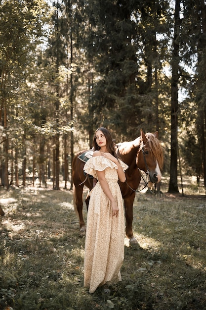 Une belle jeune fille vêtue d'une robe se tient près d'un cheval dans la forêt