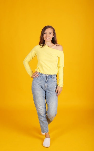 une belle jeune fille vêtue d'une veste jaune et d'un jean pose sur un fond jaune