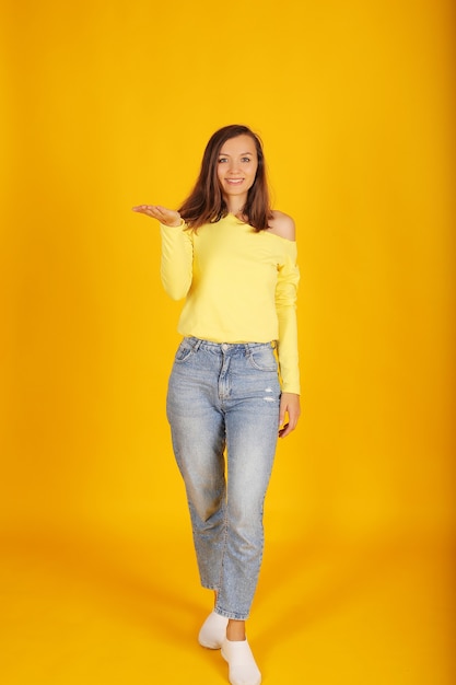 une belle jeune fille vêtue d'une veste jaune et d'un jean regarde la caméra sur fond jaune