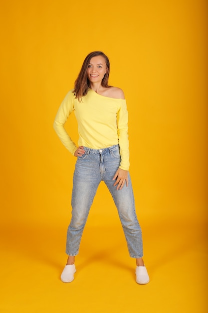 une belle jeune fille vêtue d'une veste jaune et d'un jean regarde la caméra sur fond jaune