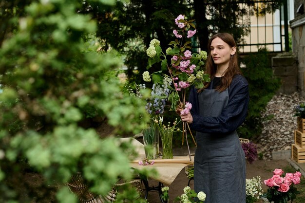 Belle jeune fleuriste sur une terrasse verdoyante fait un bouquet