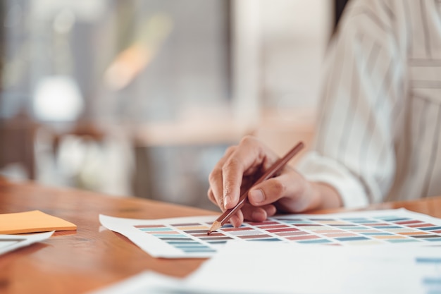 Belle jeune graphiste pigiste choisissant des échantillons de couleurs pour la conception de disposition d’écrans d’applications mobiles au bureau moderne.