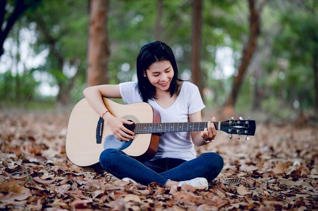 Belle jeune guitariste jouant de la guitare avec bonheur dans le jardin, forêt naturelle, concept musical