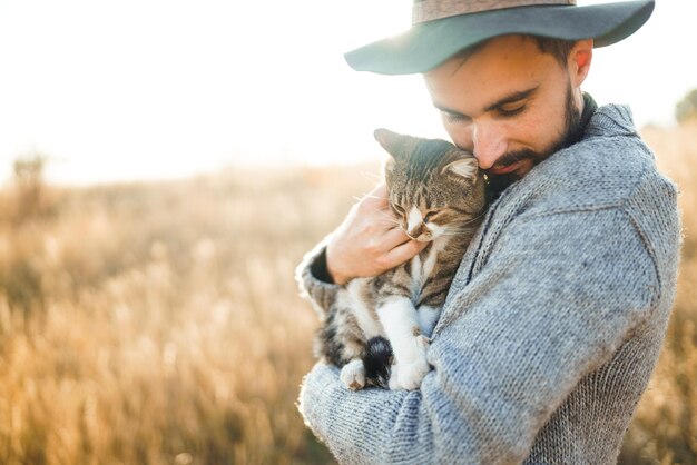 Belle jeune hipster avec un chat Un gars avec une moustache et un beau sourire étreint un chat