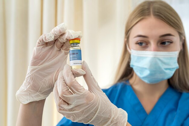 Belle jeune infirmière en gants tenant un vaccin dans ses mains pendant une pandémie. Concept de vaccination pendant une pandémie