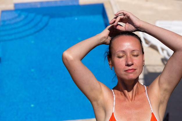 Une belle, jeune et jolie brune en maillot de bain rouge se détend dans une piscine aux eaux bleues.