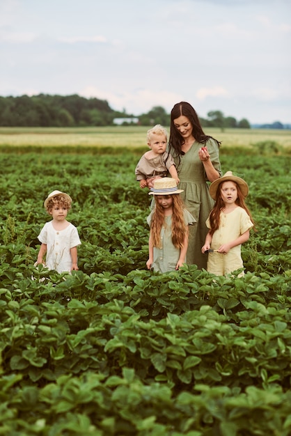 Belle jeune maman caucasienne avec des enfants dans une robe en lin avec un panier de fraises rassemble une nouvelle récolte et s'amuse avec les enfants