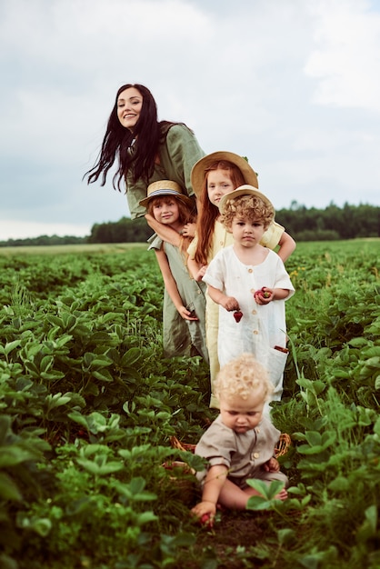 Belle jeune maman avec des enfants dans une robe en lin avec un panier de fraises rassemble une nouvelle récolte et s'amuse avec les enfants