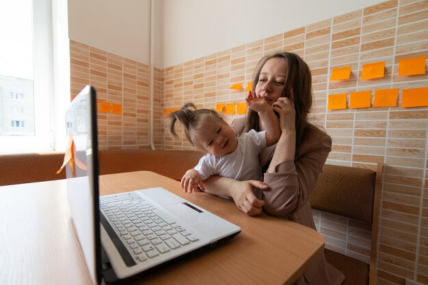 Belle jeune maman essaie de travailler à distance. Sa petite fille la dérange.