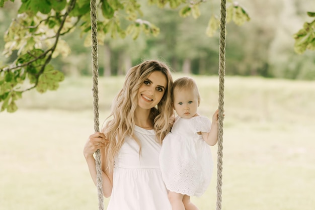 Belle jeune maman avec une fille d'un an dans la nature, maman et fille à cheval sur une balançoire