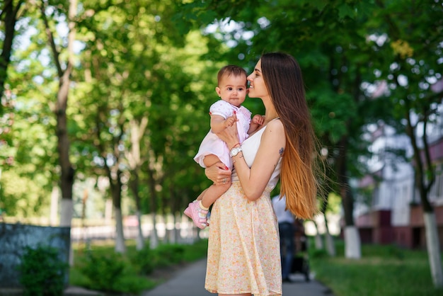 Une belle jeune maman avec une petite fille dans les mains marchant dans le parc.