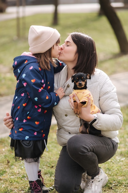 Belle jeune maman à pied avec sa fille et son petit chien famille heureuse marchant à l'extérieur avec animal de compagnie pendant