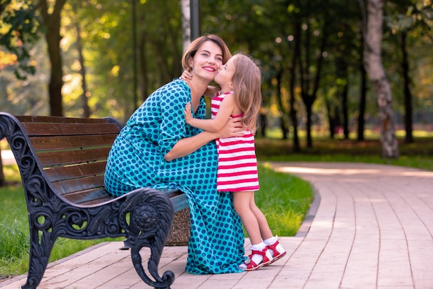 Belle jeune maman et sa fille dans une chaude journée d'été ensoleillée. Heureuse mère de famille et enfant petite fille jouant et marchant dans le parc et profiter de la belle nature.