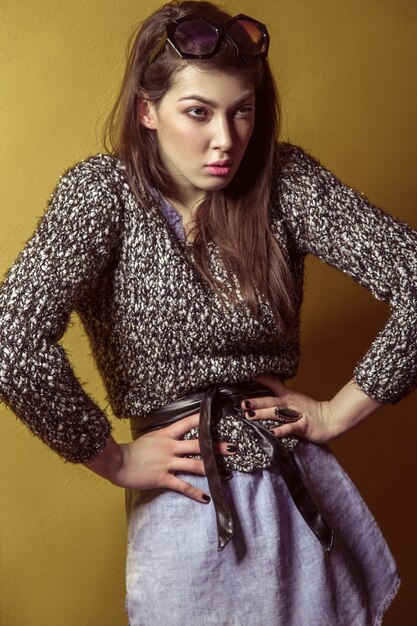 Belle jeune mannequin asiatique en jupe en jean bleu et chemisier noir et maquillage de mode posant assis sur un escabeau et regardant la caméra. Prise de vue en studio. Photo haute couture.