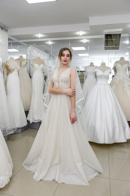 Belle jeune mariée en choisissant la robe et le voile dans le salon