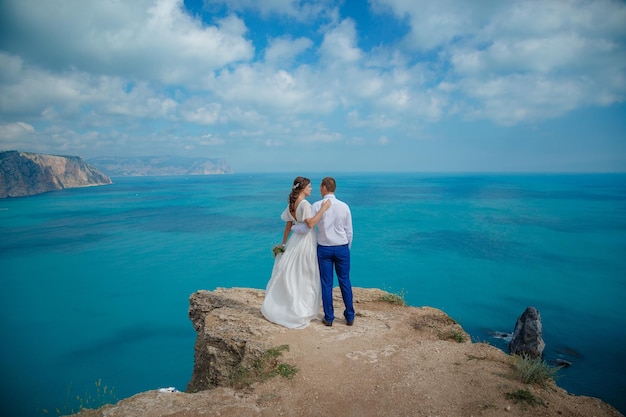 Belle jeune mariée et le marié souriants marchant sur la plage s'embrassant et s'amusant cérémonie de mariage près des rochers et de la mer Cérémonie de mariage sur la côte de Chypre