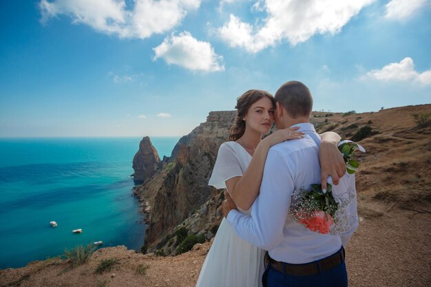 Belle jeune mariée et le marié souriants marchant sur la plage s'embrassant et s'amusant cérémonie de mariage près des rochers et de la mer Cérémonie de mariage sur la côte de Chypre