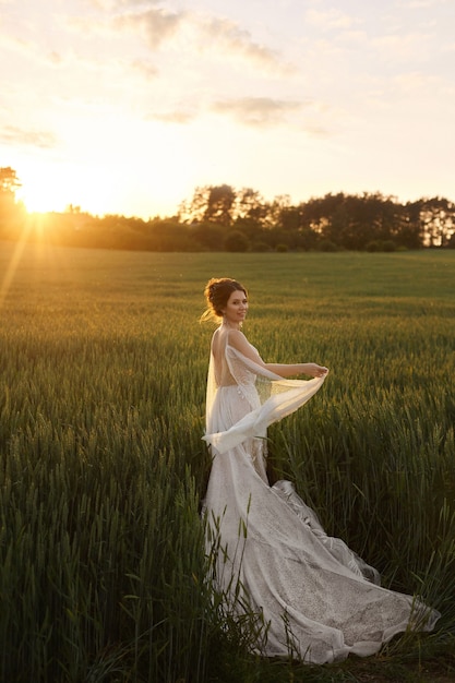 Belle jeune mariée en robe de mariée en dentelle sur le terrain au coucher du soleil