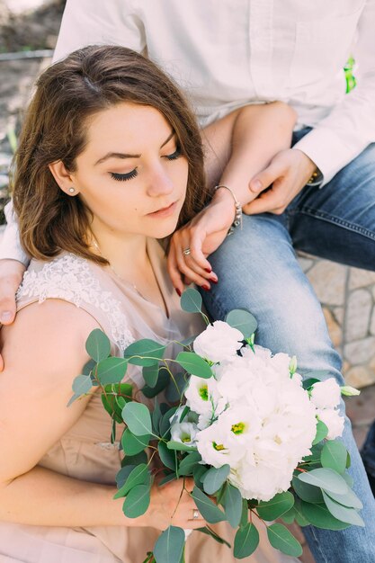 La belle jeune mariée songeuse s'assied à côté du marié tenant un bouquet blanc des fleurs