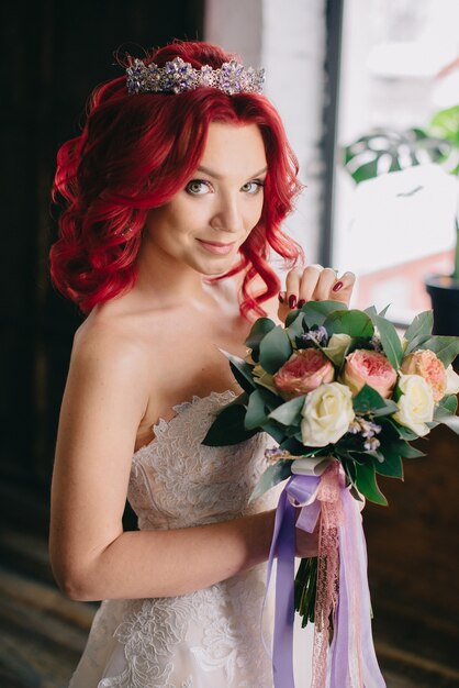 Belle jeune mariée tenant un bouquet et debout près de la fenêtre dans le grenier