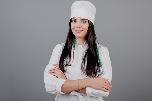 Belle jeune médecin souriant en peignoir médical isolé sur gris