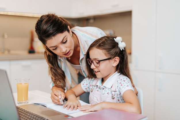 Belle jeune mère aidant sa fille cadette à faire ses devoirs.