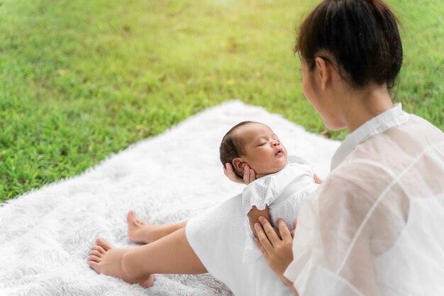 Belle jeune mère asiatique tenant son nouveau-né dort et se sent avec amour et toucher doucement, puis assis sur l'herbe verte dans le parc