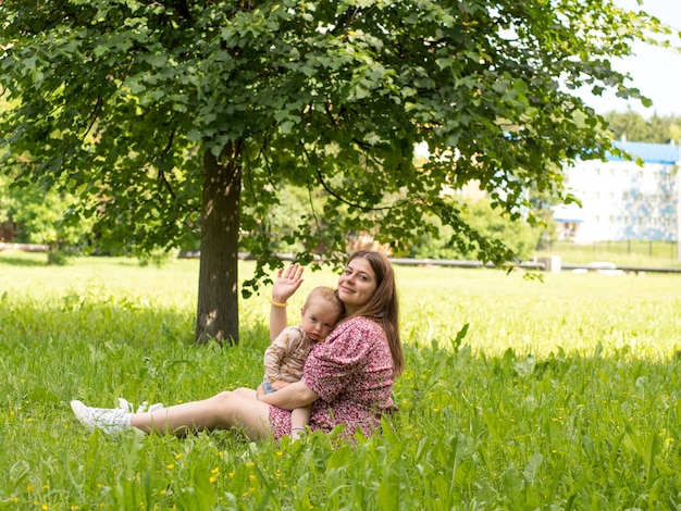 Belle jeune mère avec un bébé dans ses bras est assise dans le parc sur l'herbe par une journée ensoleillée