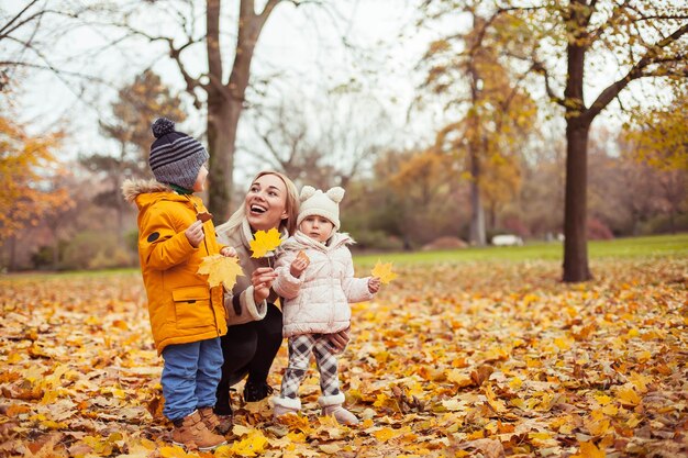 Une belle jeune mère et deux petits enfants se promènent dans le parc d'automne. Maman et deux petits enfants jouent. Hiver chaud. Automne lumineux. Confortable.