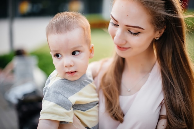 Une belle jeune mère embrasse et embrasse son petit fils pendant le coucher du soleil dans le parc. Bonne promenade en famille dans le parc.