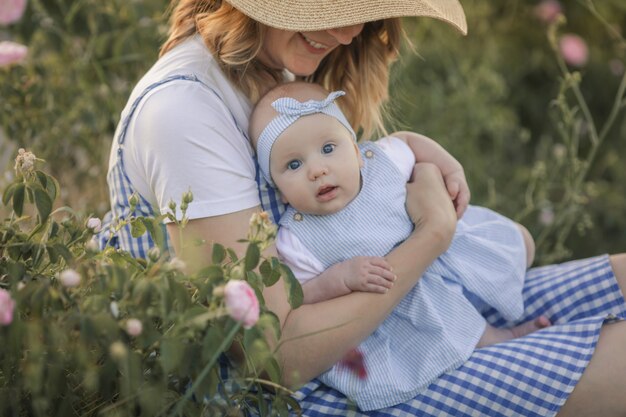 Belle jeune mère avec un enfant se dresse dans un champ agricole avec une rose en fleurs