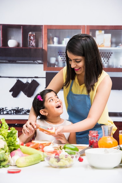 Belle jeune mère et fille indienne ou asiatique en cuisine, avec table pleine de fruits et légumes