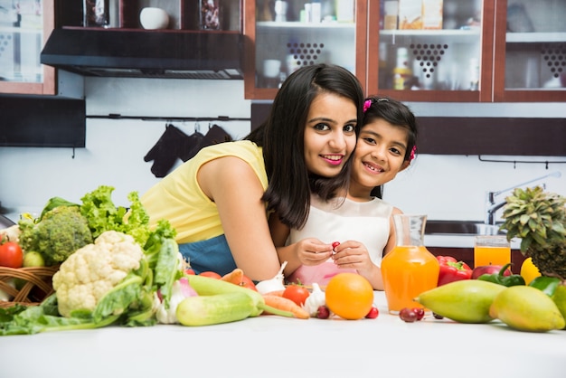 Belle jeune mère et fille indienne ou asiatique en cuisine, avec table pleine de fruits et légumes