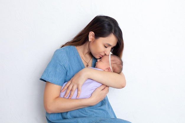 Belle jeune mère avec une fille nouveau-née dans une couche sur un fond blanc Tendresse de la maternité Espace pour le texte