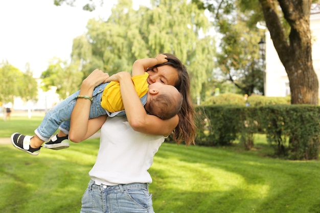 une belle jeune mère hugsher petit fils dans un t-shirt jaune et un jean dans le parc