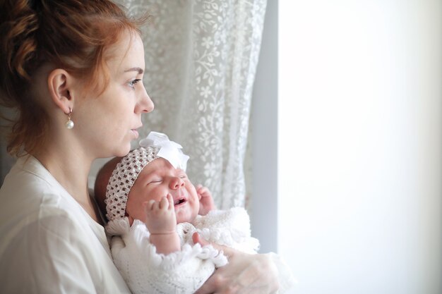 Belle jeune mère et nouveau-né dans ses bras debout près de la fenêtre