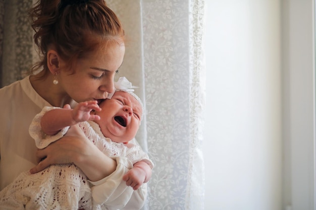 Belle jeune mère et nouveau-né dans ses bras debout près de la fenêtre