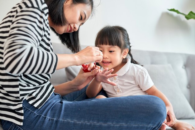 Belle jeune mère peint le vernis à ongles à sa petite fille mignonne