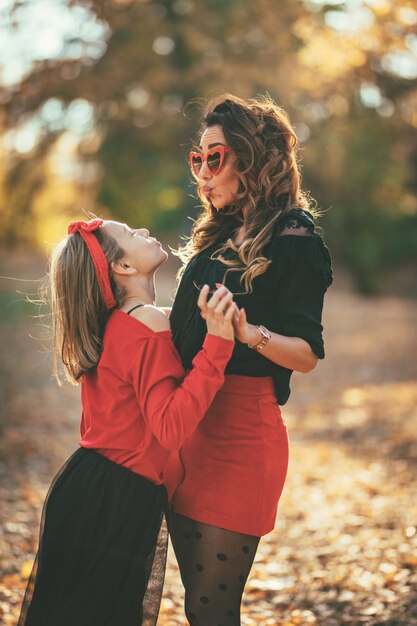 Belle jeune mère et sa fille heureuse s'amusant dans la forêt au coucher du soleil. Ils s'embrassent, se sourient et se regardent.