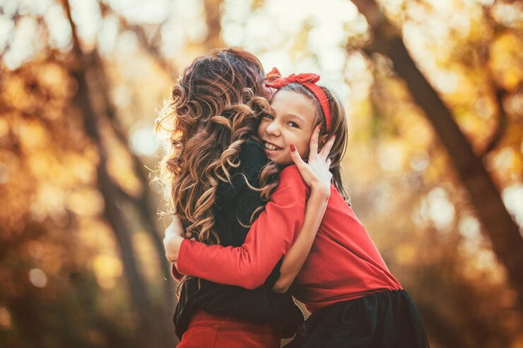 Belle jeune mère et sa fille heureuse s'amusant dans la forêt au coucher du soleil. Ils s'embrassent et sourient.
