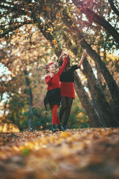 Belle jeune mère et sa fille heureuse s'amusent dans la forêt au coucher du soleil. Ils se tiennent la main, rient et sautent.