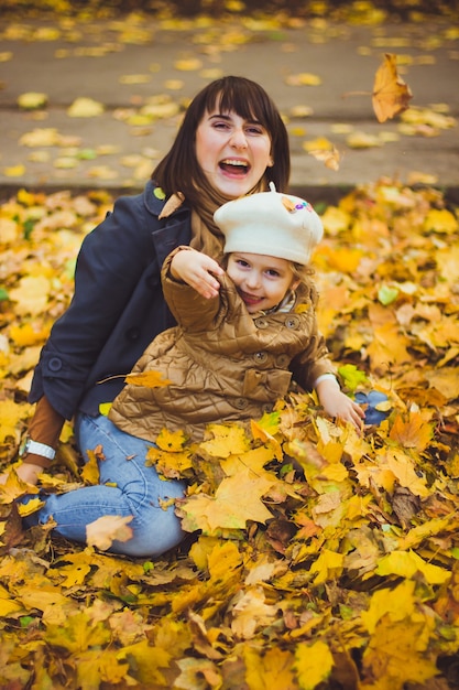 Belle jeune mère et sa fille heureuse s'amusent dans la forêt à l'automne. Promenades dans un parc d'automne avec les enfants. La famille passe du bon temps à jouer avec les feuilles tombées.