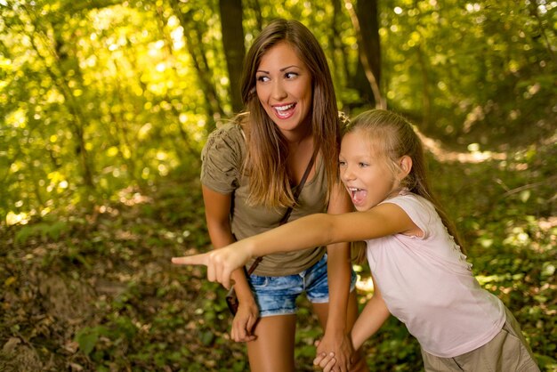 Belle jeune mère et sa fille marchant à travers la forêt. Petite fille pointant du doigt loin.