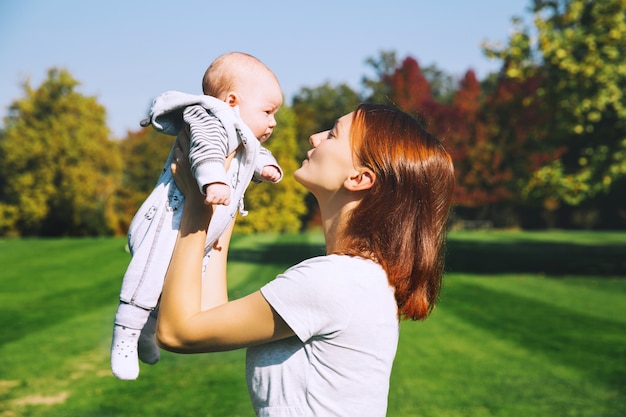 Belle jeune mère tenant dans les bras son bébé dans le parc en automne. Maman heureuse avec son enfant sur la nature.