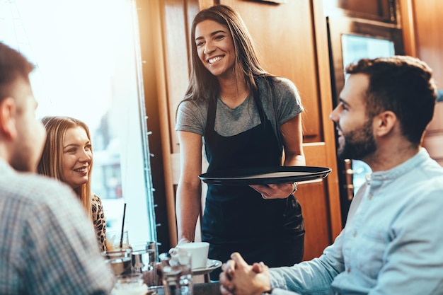 Une belle jeune serveuse sert un groupe de jeunes amis souriants dans un café.