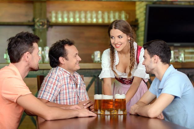 Belle jeune serveuse servant de la bière alors que trois hommes.