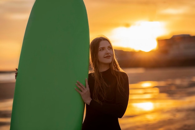 Une belle jeune surfeuse pose avec une planche de surf sur la plage au coucher du soleil