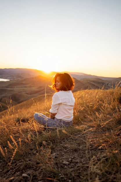 Une belle jeune touriste est assise au sommet d'une montagne et profite de la vue sur le coucher de soleil