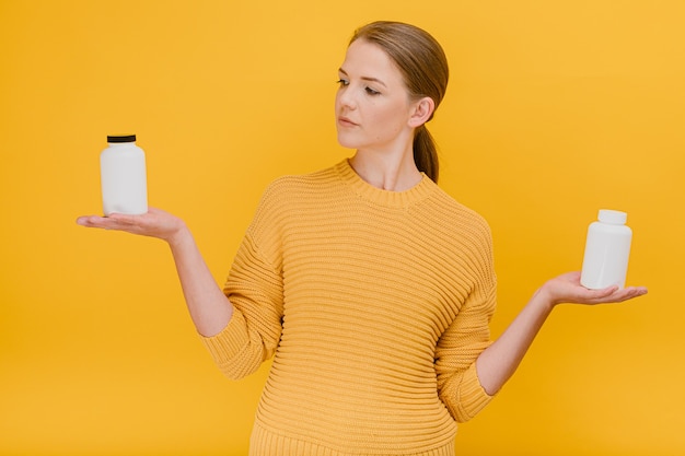 Belle jolie femme choisissant une bouteille de pilules médicales ou de vitamines habillées avec désinvolture ayant un traitement d'expression douteux et un concept de prévention des maladies