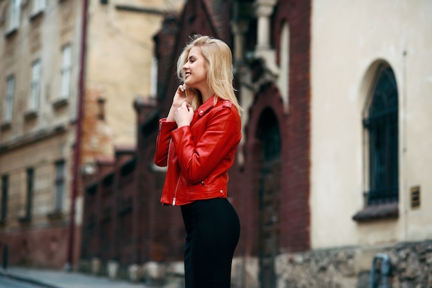 Belle jolie fille blonde souriante avec une silhouette parfaite dans une veste en cuir rouge et une jupe noire serrée